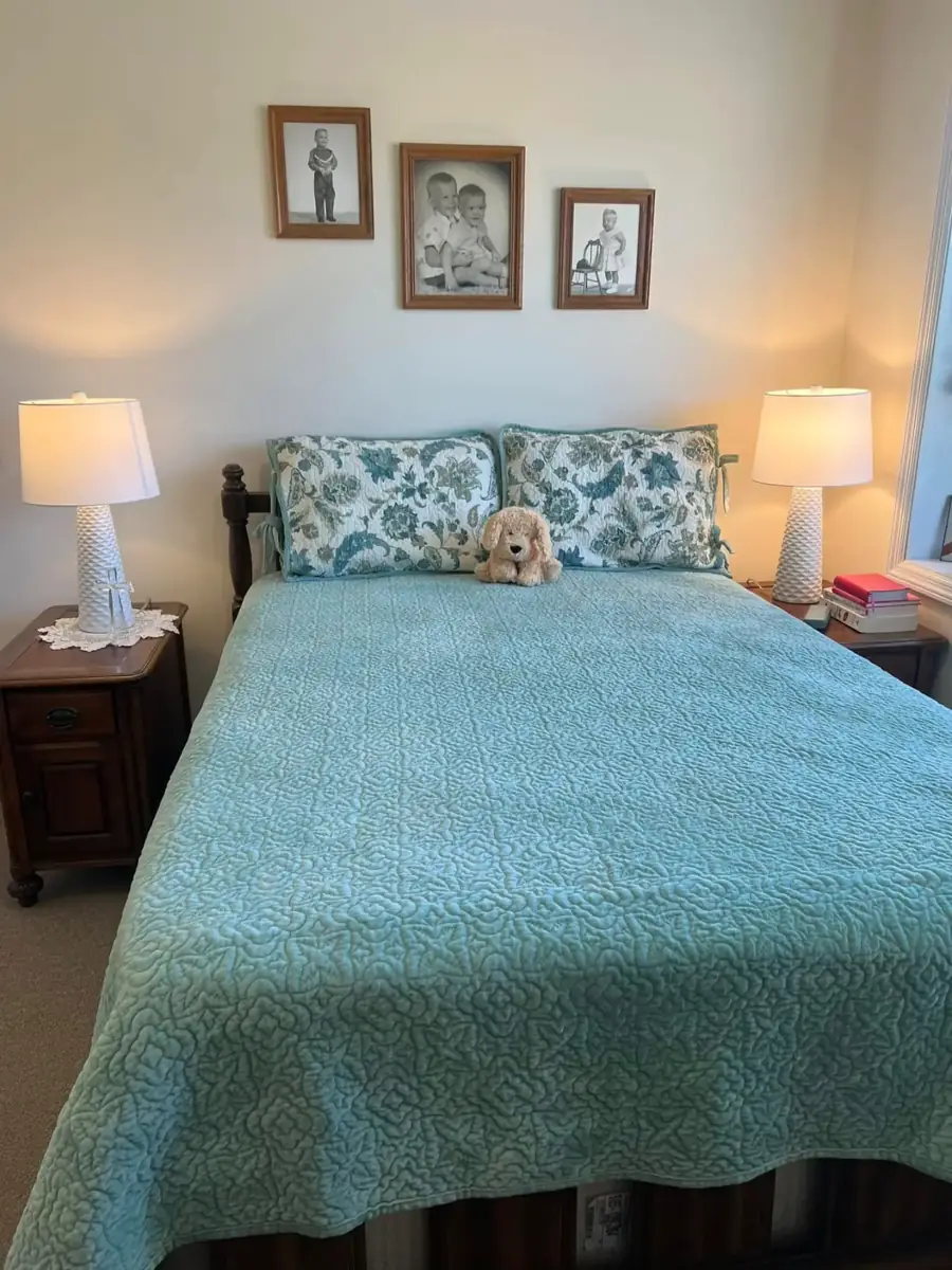 A bed with a blue spread and family photographs hung above it