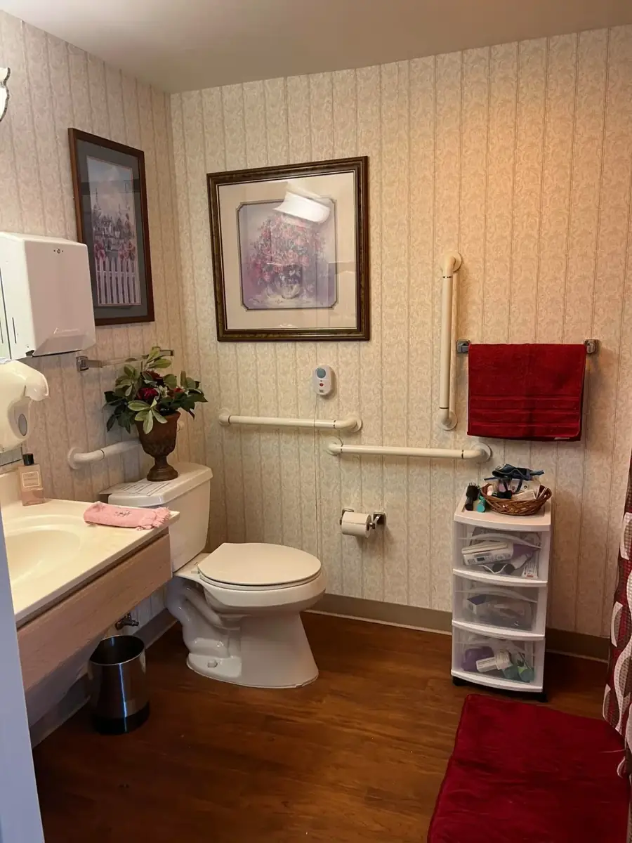 A bathroom with grab bars, framed pictures and a red towel
