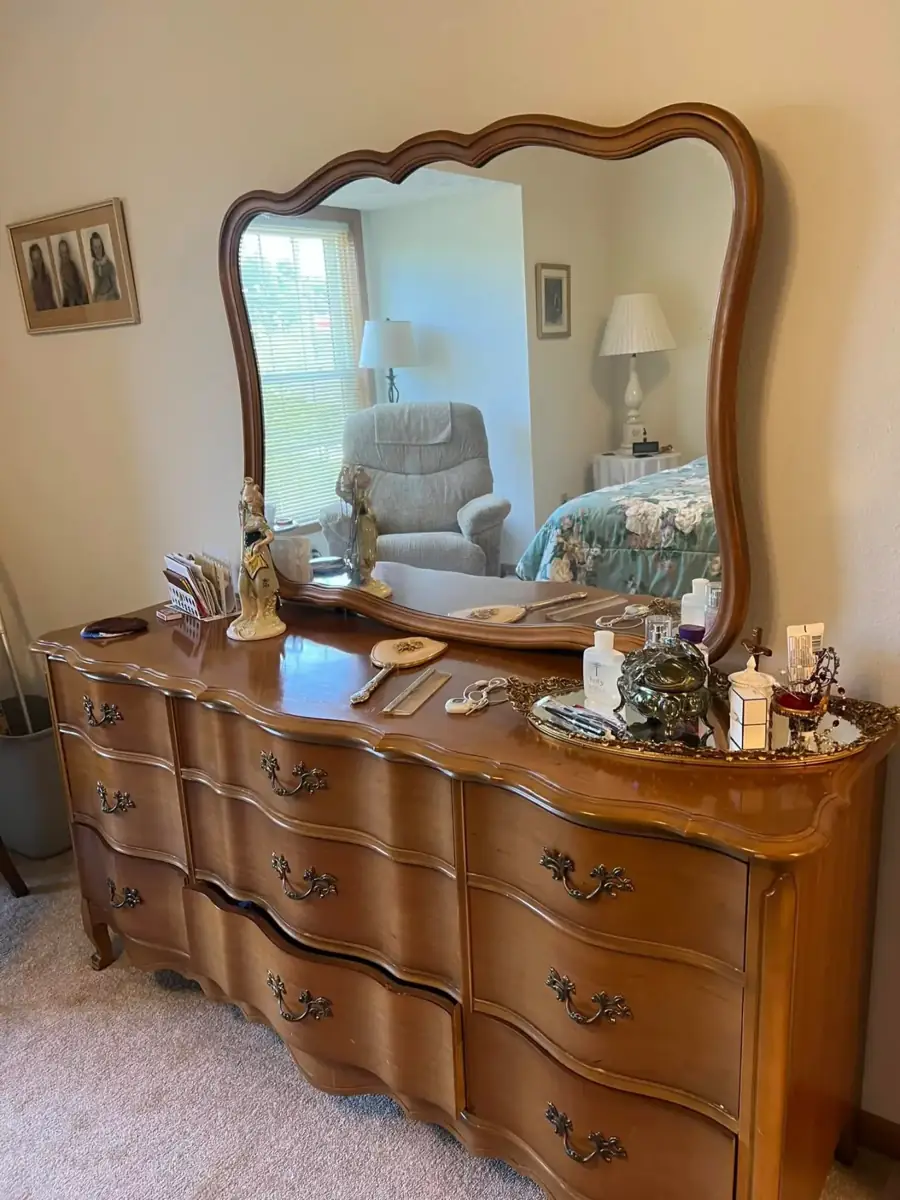 A wooden dresser with a curved mirror and keepsakes on top