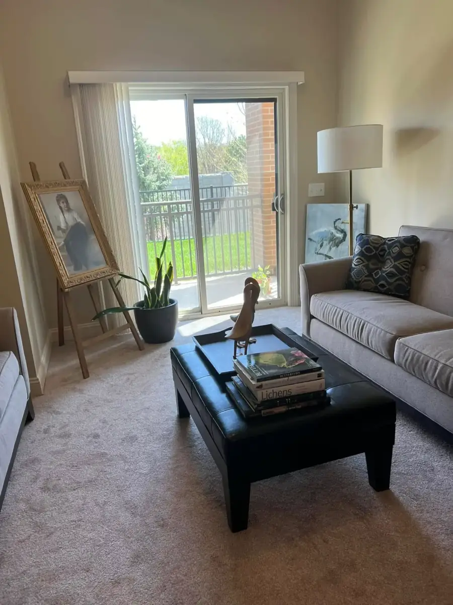 A sitting area with a sofa, leather ottoman and a framed portrait on an easel