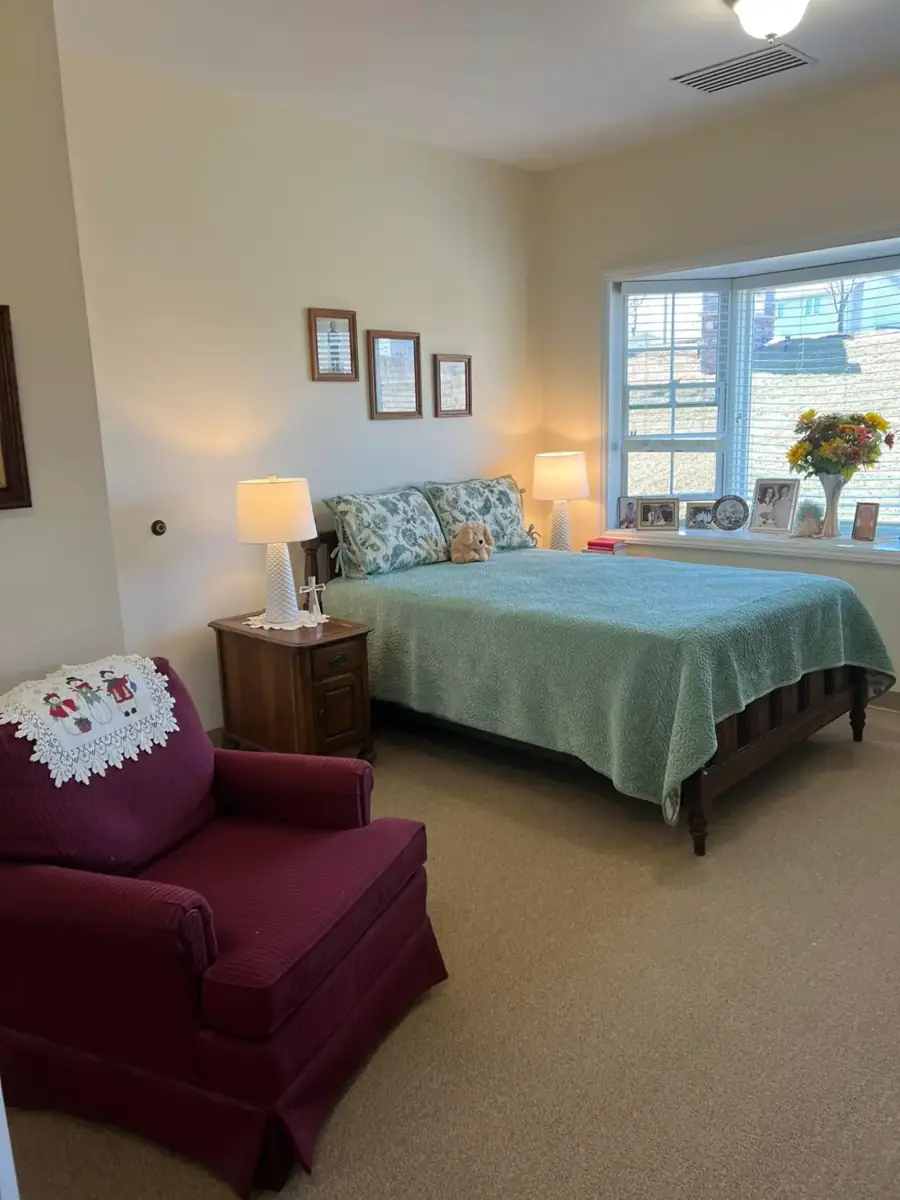A bedroom with a green bedspread, a red armchair and flowers by the window